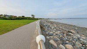 Image shows a wide path with the sea to the right and green grassy area to the left