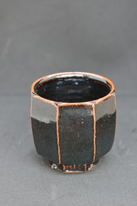 Ceramic faceted dark cup with orange accents and shiny gaze