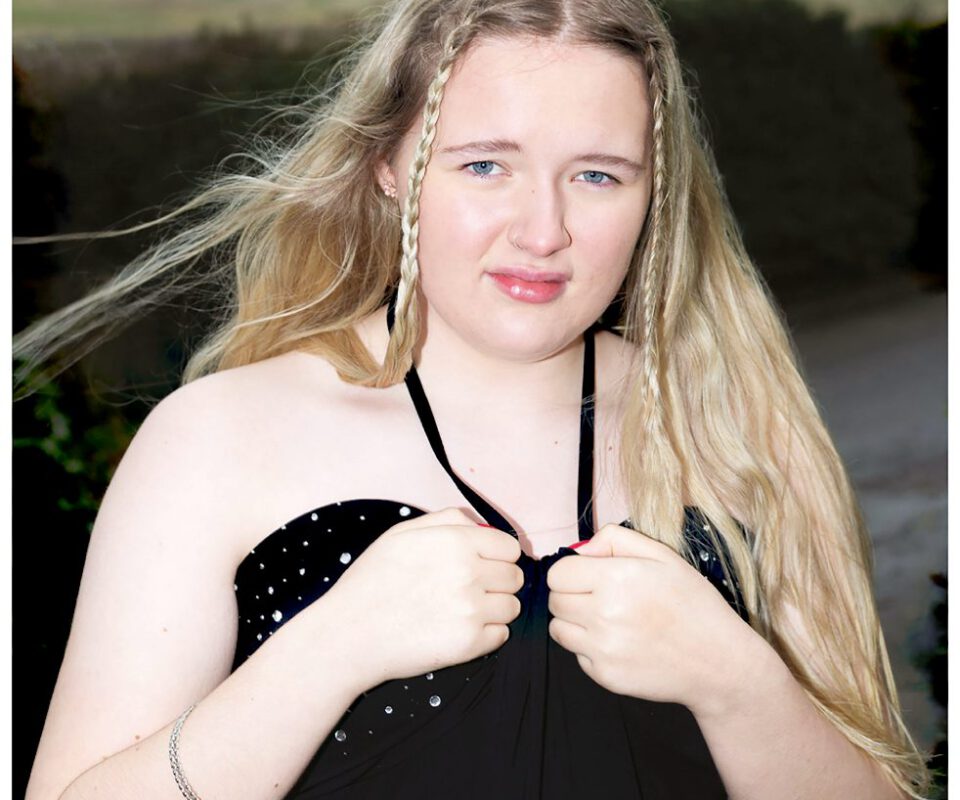Image shows a photo by Fran Rowse of a young white woman with long blond hair wearing a black halterneck dress