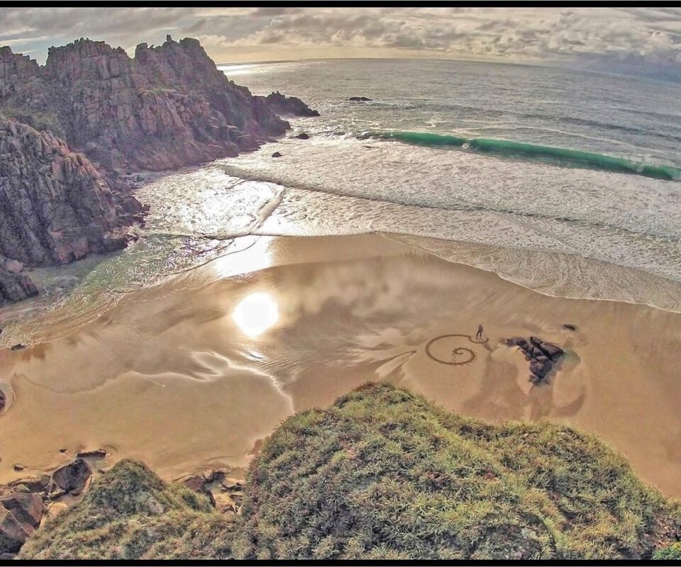 Looking down on a sandy beach where a small figure is creating patterns in the sand