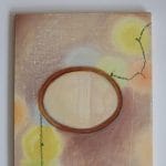 Beth Kaye - Glowing is a painting with a wooden oval frame on a textured background, featuring blurred yellow circles and a looping green string, creating a soft, dreamy atmosphere.