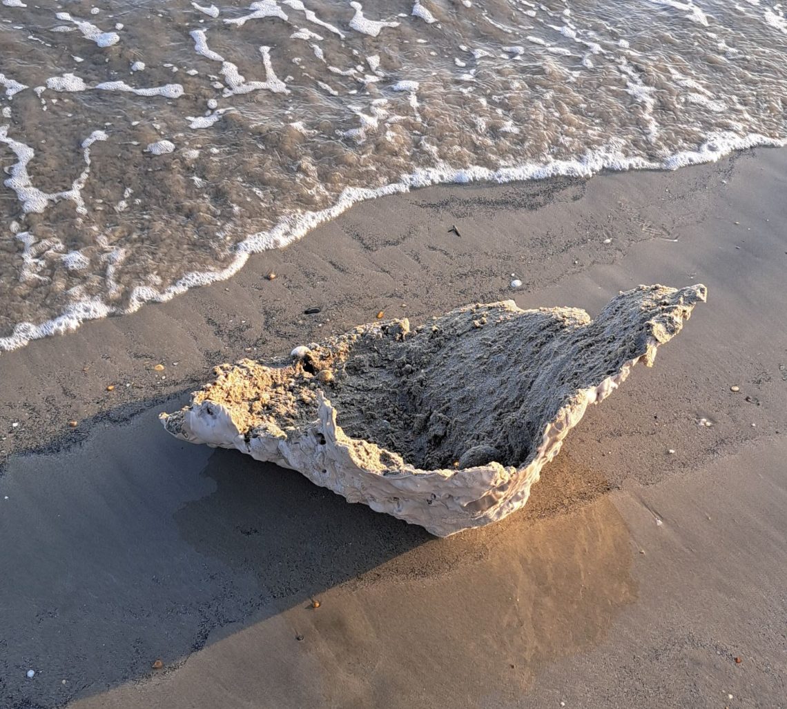 Image shows a cast of sandcastle lying on a sandy beach