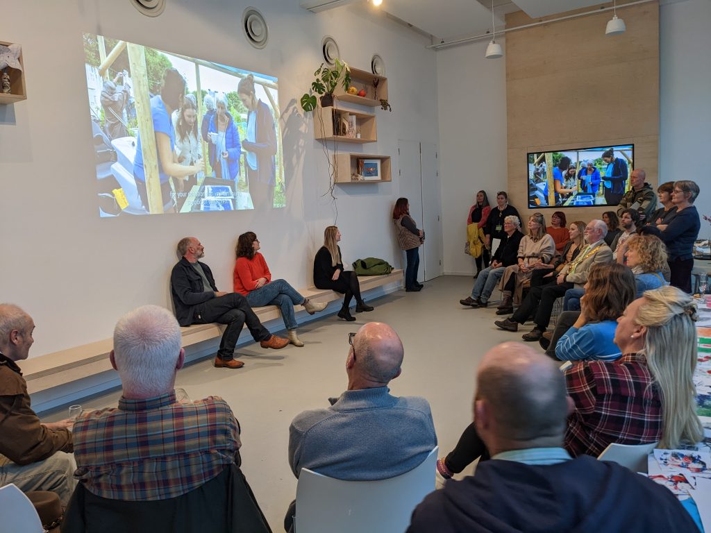 Image shows a group of seated people looking at a presentation projected on to a wall