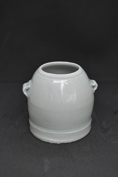 small round cream porcelain vase with small handles on black background