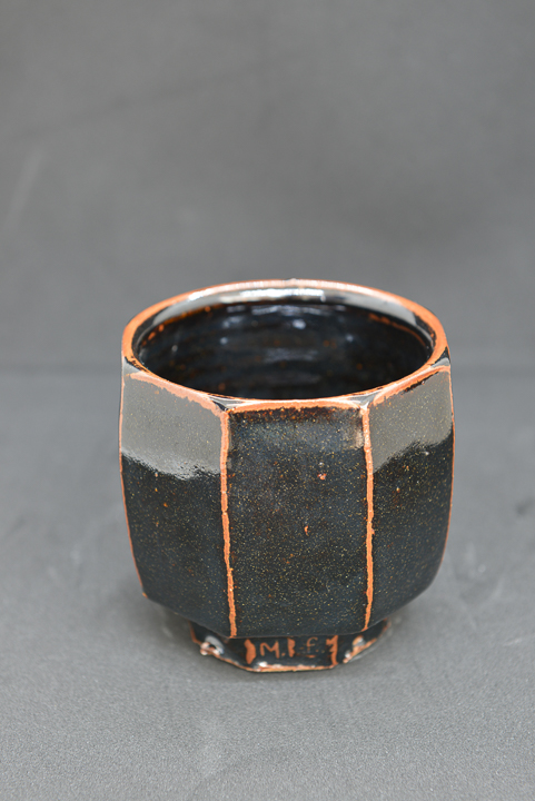 Ceramic faceted dark cup with orange accents and shiny gaze