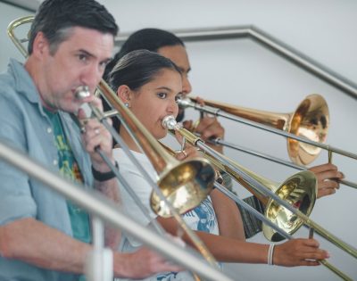 Image shows a group of musicians playing trombones