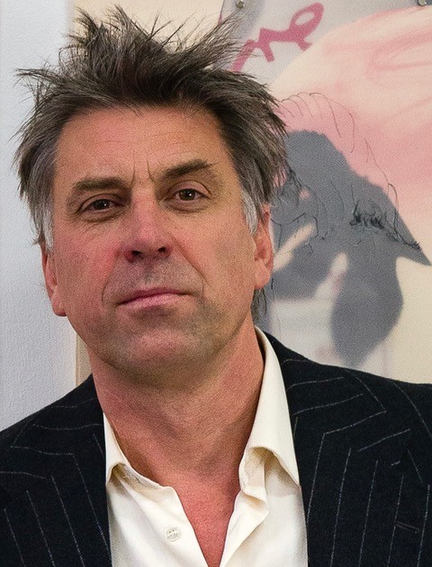 Image shows a heald and shoulders shot of a white male wearing a light open necked shirt and a dark jacket