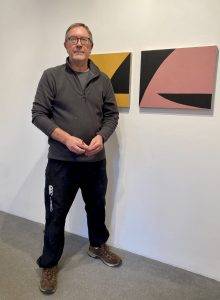 Image shows a white mail standing in front of abstract paintings on a wall